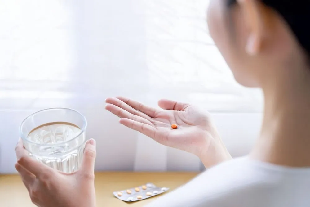 後ろから撮影された女性が、左手に水の入ったコップ、右手に薬を持ち、飲もうとしている様子。妊娠中絶薬の腎不全リスクをテーマにしたイメージ。