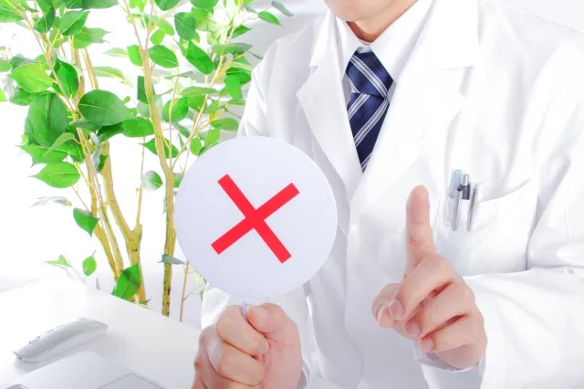 白衣の医師がバツ印を掲げ、責任のない態度を批判するジェスチャー