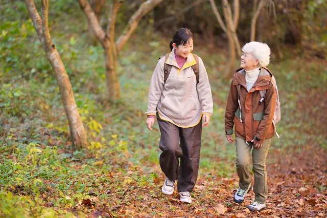 落ち葉の山道を笑顔で歩く白髪のお母さんと娘が会話しながら元気に散策している様子