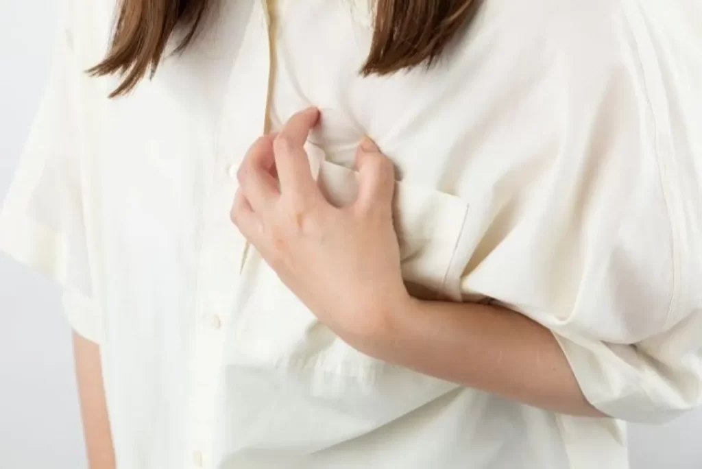 心臓のあたりを左手で押さえる女性の手元クローズアップ（心臓疾患の症状イメージ）