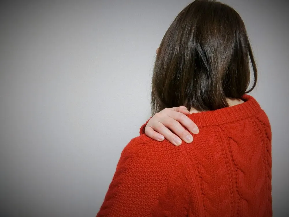 赤いセーターを着た女性が背中の痛みで肩を押さえている様子