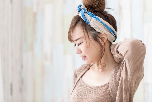 ヘアバンドを着けた女性が首の痛みで左手で首を押さえる様子