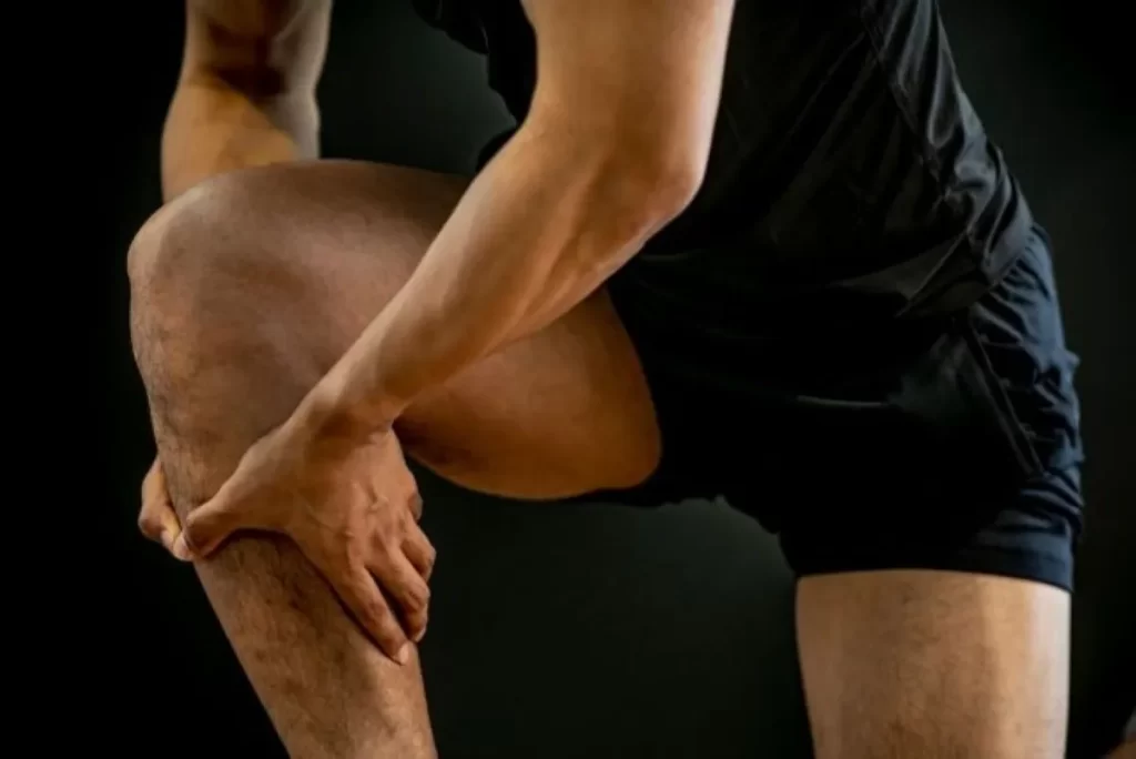 右ふくらはぎの肉離れで痛みを感じ、両手でふくらはぎを押さえる男性の写真（黒背景）