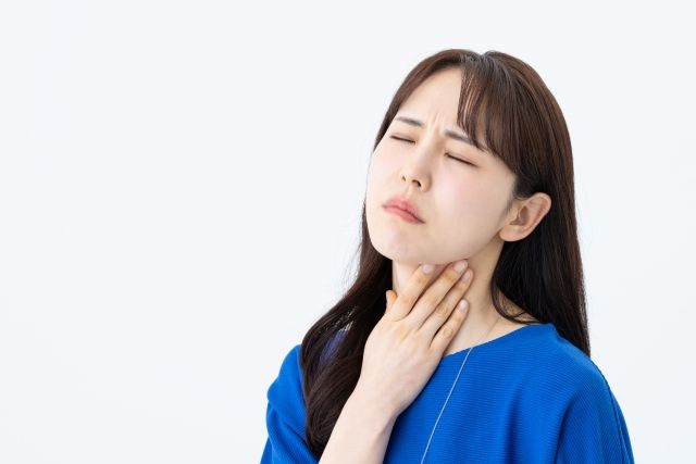 青い服を着た女性が喉の痛みや違和感を感じて辛そうに喉を触っている様子