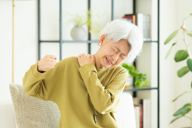 白髪の女性が右肩の痛みで左手で肩を押さえている様子