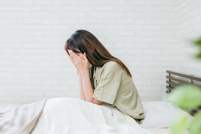 不眠症に悩む女性がベッドに座り、顔を両手で抑えている様子