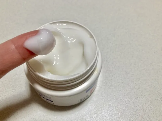 左の人差し指にステロイド軟膏を塗っている様子で、隣に軟膏のチューブが置かれている画像