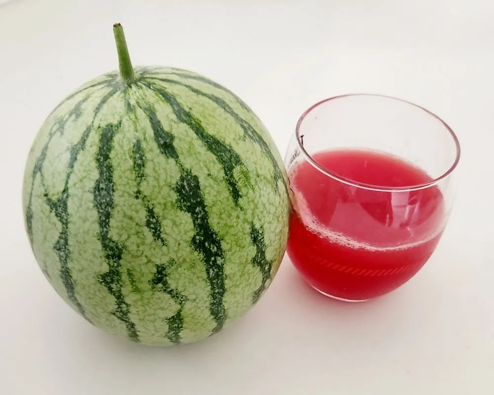 丸ごとのスイカと透明なグラスに注がれた赤いスイカジュースが並んでいる画像