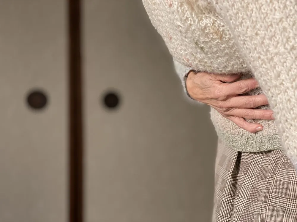 高齢女性がセーターを着て腹痛でお腹を抑えている両手のクローズアップ画像