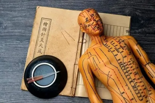 古い中医典籍の上に横たわるツボ人形と、隣に置かれた鍼の容器