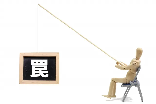 木製の人形が釣り竿で釣りをしている先にある「罠」と書かれた看板のイラスト