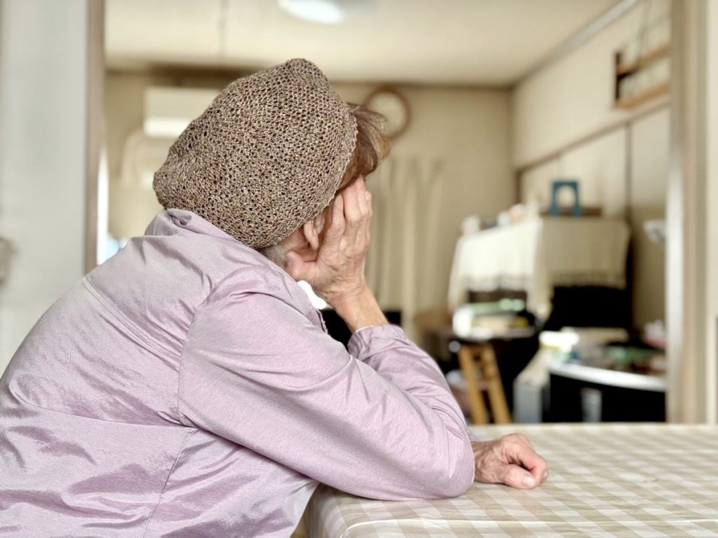 70歳以上のやせた女性が片頭痛で頭を抱え、苦しむ背中の様子