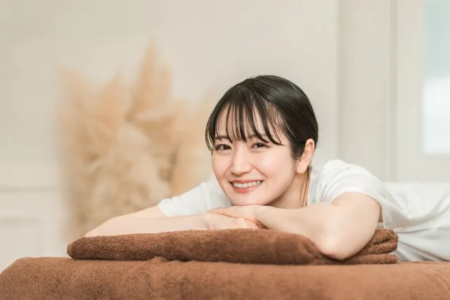 鍼治療後の施術ベッドでうつ伏せになり、笑顔でリラックスする女性(茶色のシーツ)