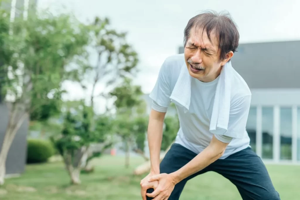 80歳男性が膝の痛みでしゃがみ込み、右膝を両手で押さえている様子