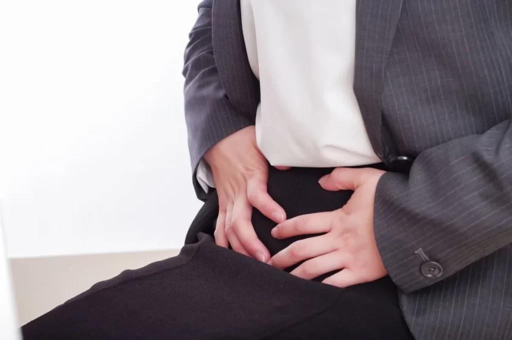 生理痛や子宮腺筋症で下腹部に痛みを感じ、両手で押さえている女性のクローズアップ