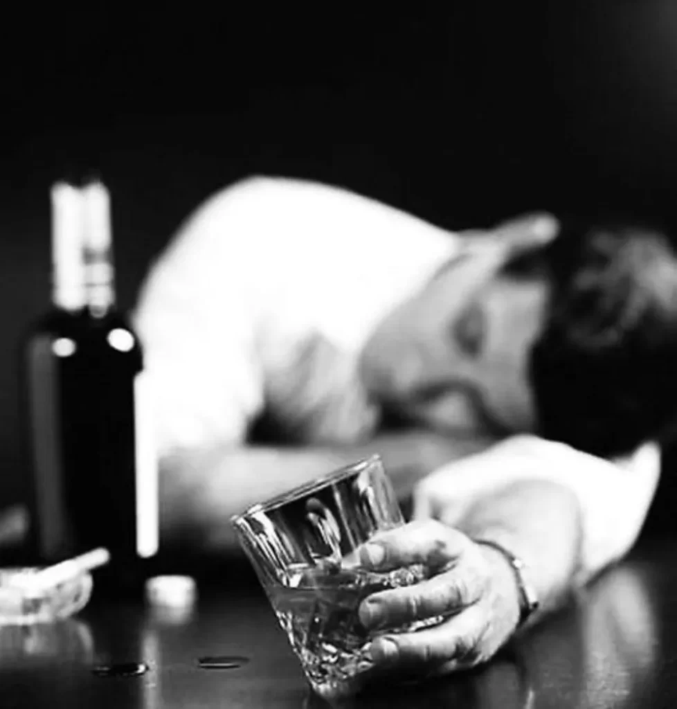 二日酔いでテーブルにうつ伏せになり、手に酒のコップを持ったサラリーマンの白黒写真