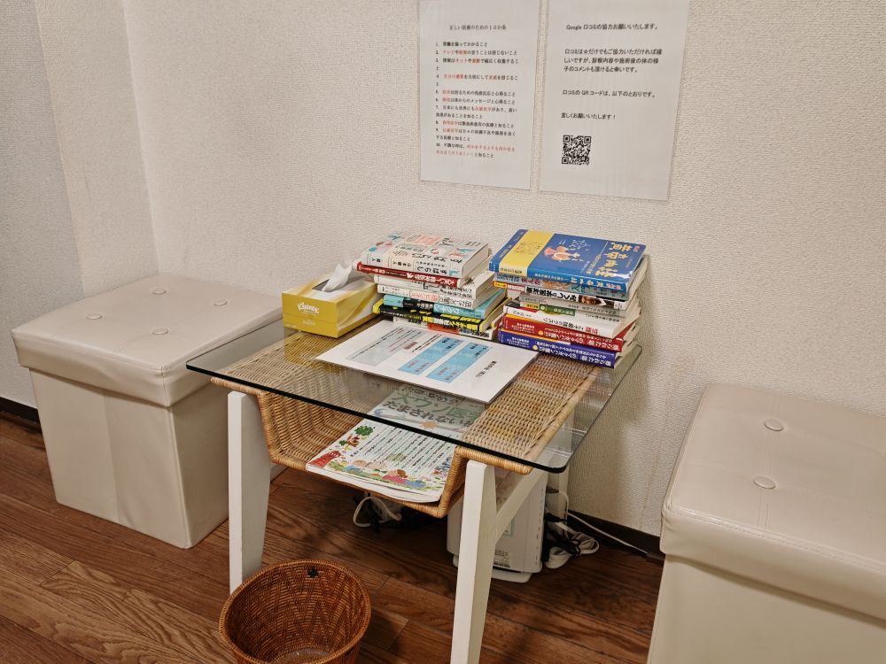 待合室の様子。低い椅子2つ、ガラステーブル、メニューと本の山、テーブル下のゴミ箱が写っている。