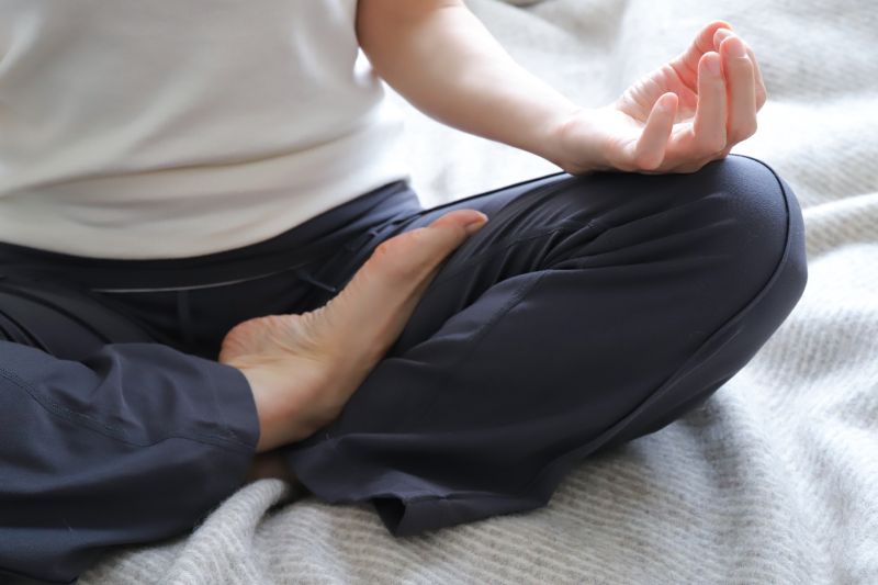 あぐらでヨガ呼吸をする女性の足と膝上の手のクロースアップ。呼吸1回で気が六寸進むことを示すイメージ