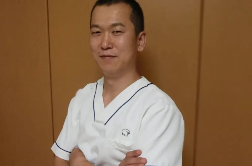 半袖の施術着を着た鍼灸師・李哲が横を向いて微笑むプロフィール写真