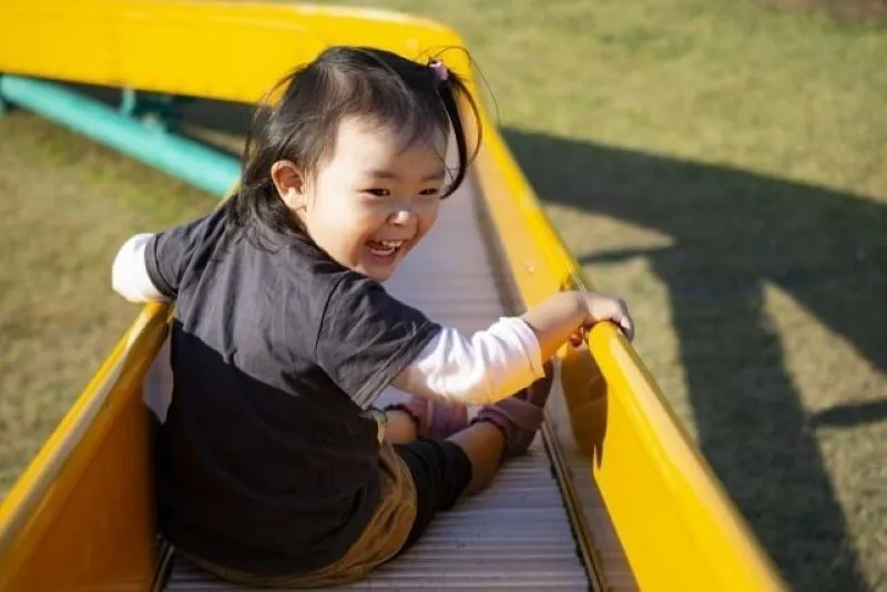 長い滑り台を滑りながら後ろを見て笑顔を見せる子ども