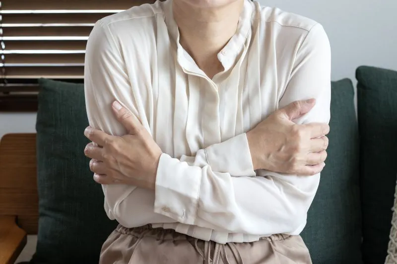 寒さで腕を抱えている女性の上半身、冷え性を示すイメージ
